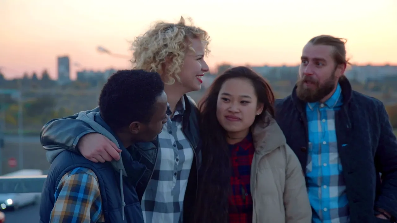 Four friends laughing, arms around each other, at dusk